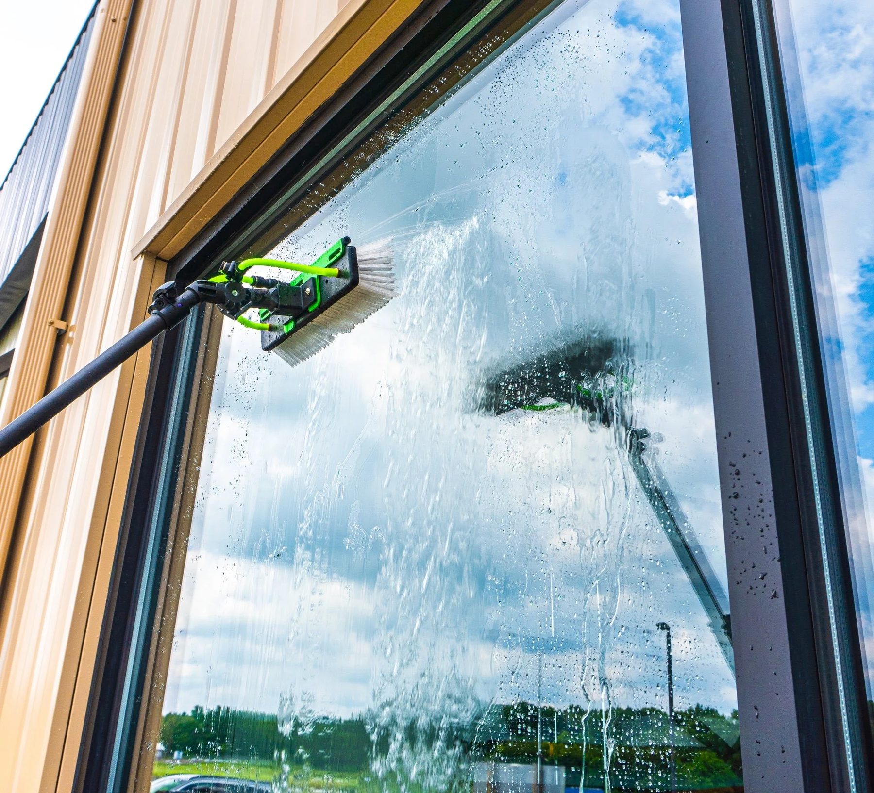 A water-fed pole brush cleaning a large picture window, blue sky reflected in the glass